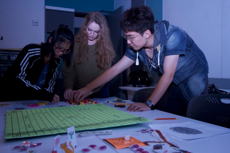 Students lean over a game board during a game design class